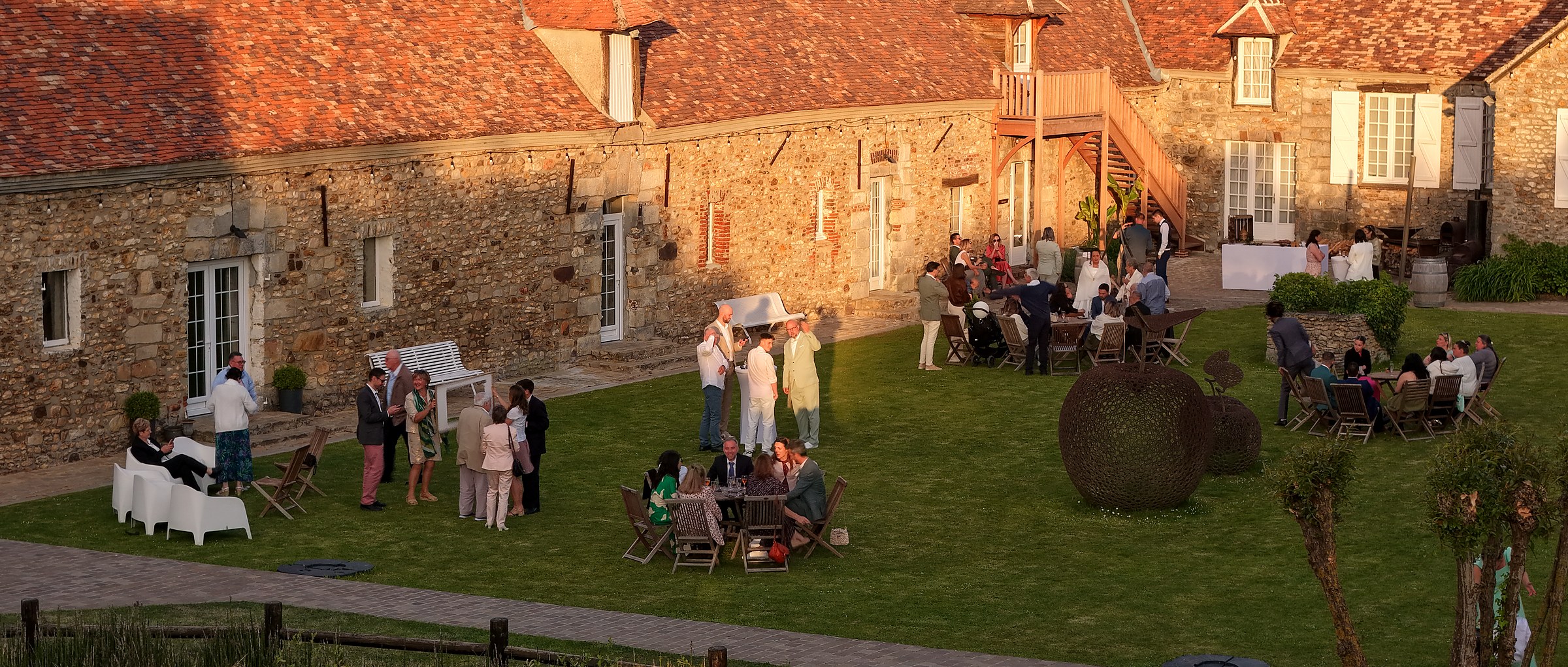 Cour intérieure pavée d'une longère pendant le vin d'honneur, heure dorée
